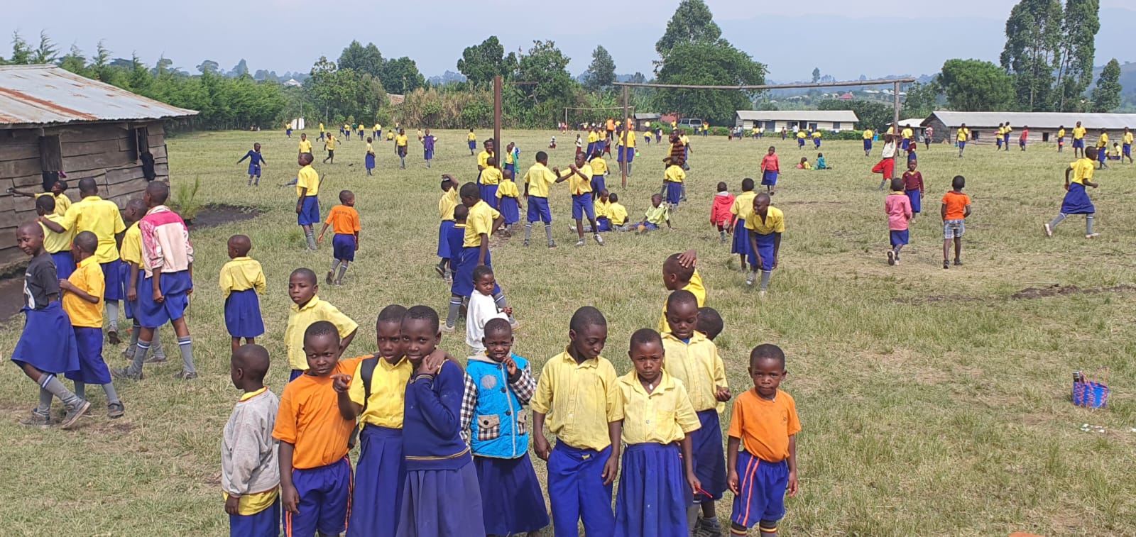Pupils in blue and yellow uniform on the school field at Nyantaboma
